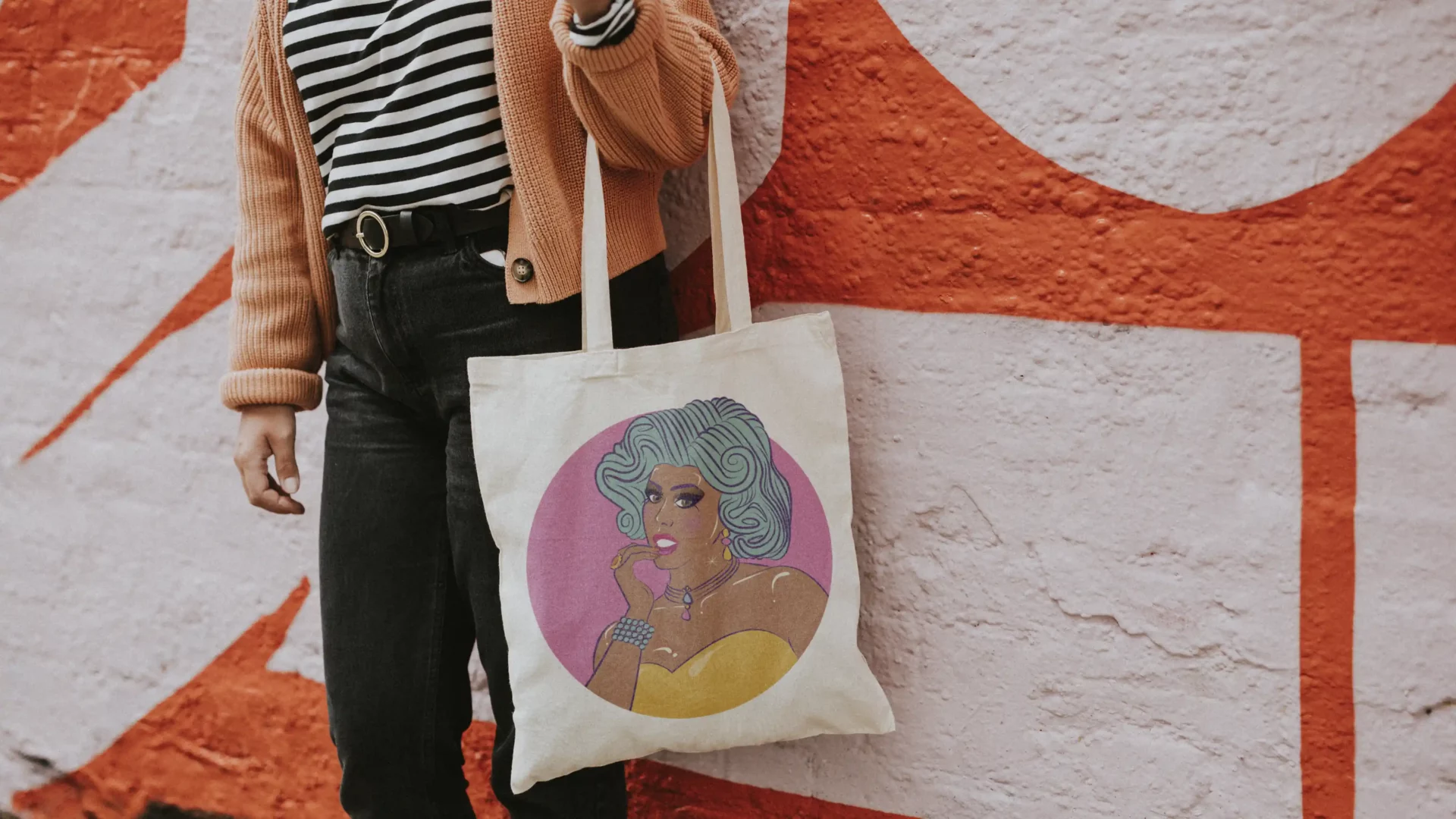 vibrant original festival branding featuring custom illustrations of performer in drag wearing fabulous oversized teal wig and yellow bustier, with fingers to lips. custom printed tote bag merchandise worn by stylish woman against a bold mural backdrop.